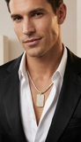 Man wearing a black suit with a white shirt and a necklace with a dog tag.